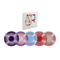 A set of five decorative plates with intricate circular patterns in purple, orange, blue, red, and white, displayed in front of a white book or album cover featuring a colorful abstract letter 'A'.
