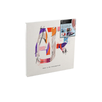 A square canvas wall art print featuring an abstract colorful letter 'A' on a light beige background, shown at an angle with a small printed insert card on the top right.